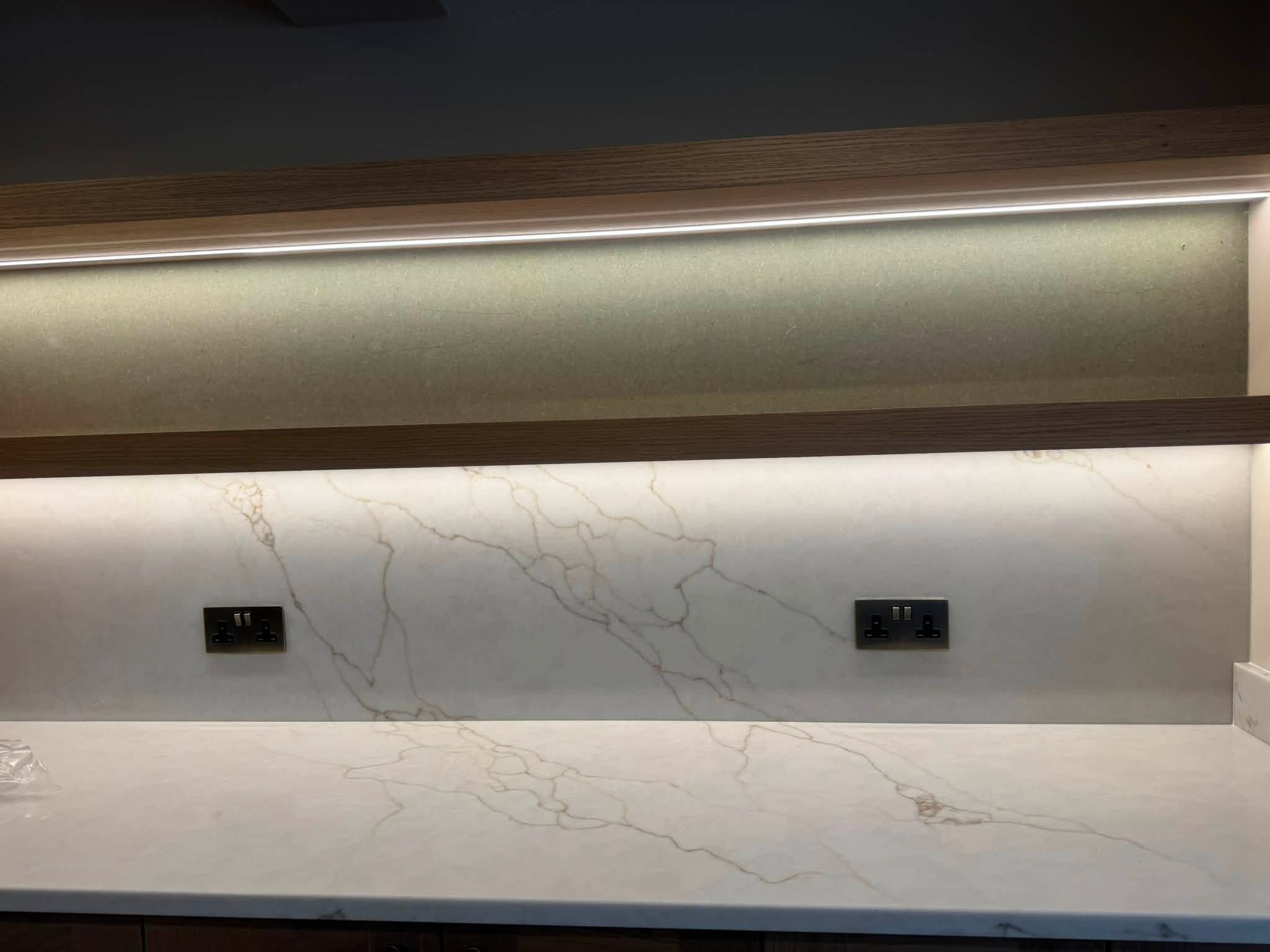 Kitchen worktop and marble splashback lit by a concealed strip light, with two double sockets