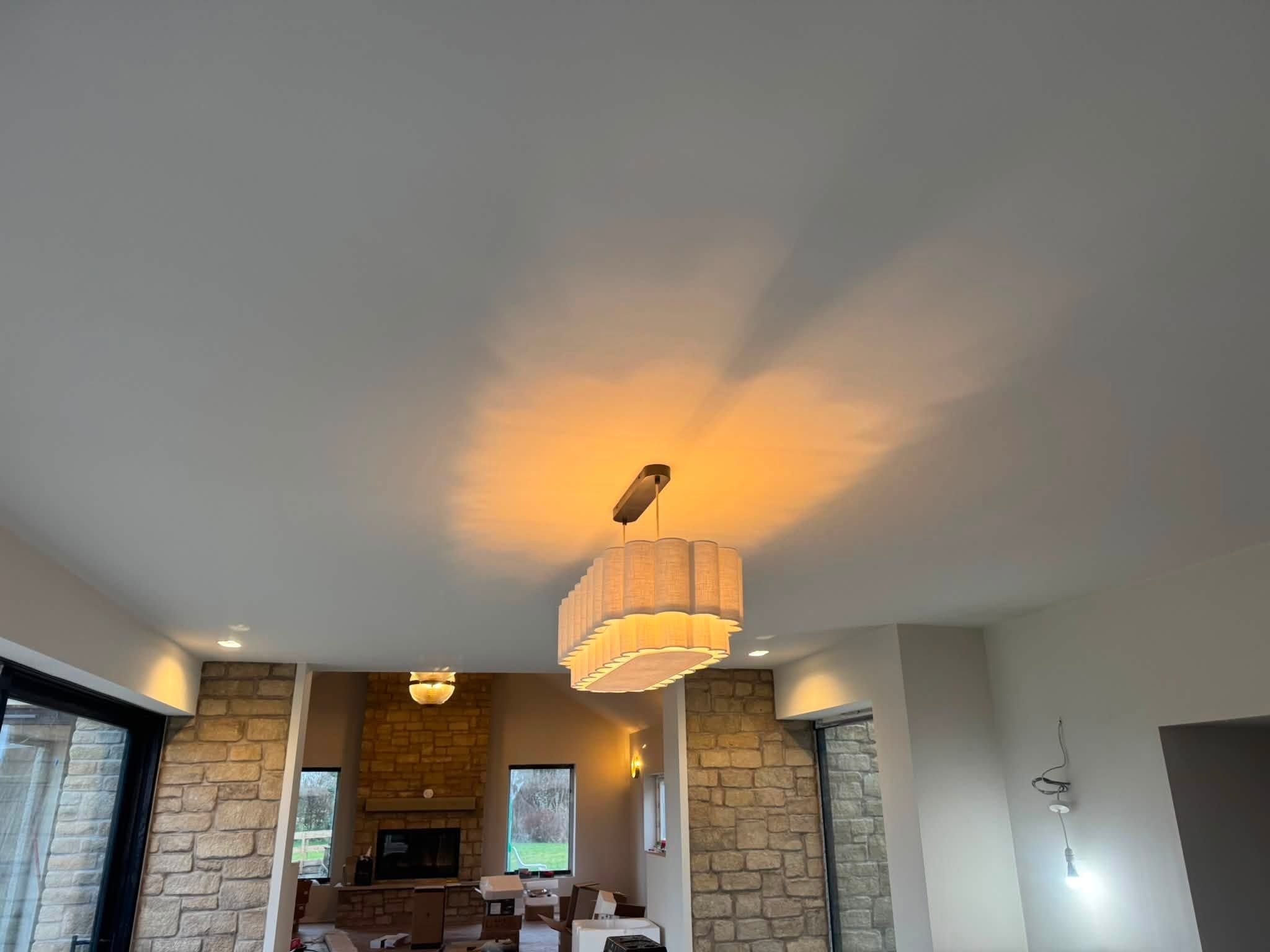 Pendant light glowing on a white ceiling in an open-plan room with stone walls