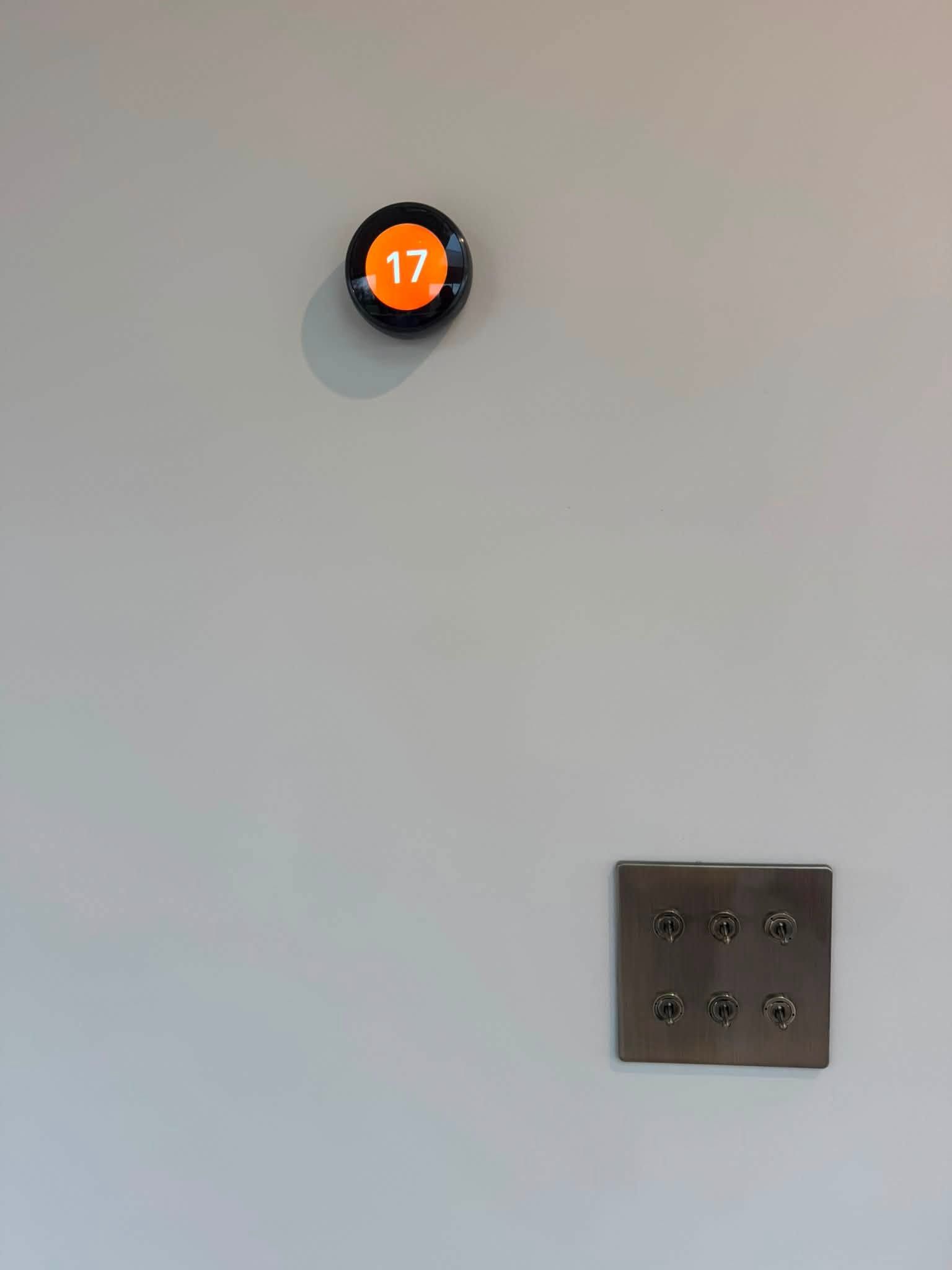 Round thermostat above a six-toggle bronze switch plate on a plain wall